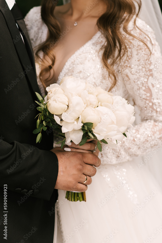 Beautiful white wedding bouquet of peonies in the hands of the bride