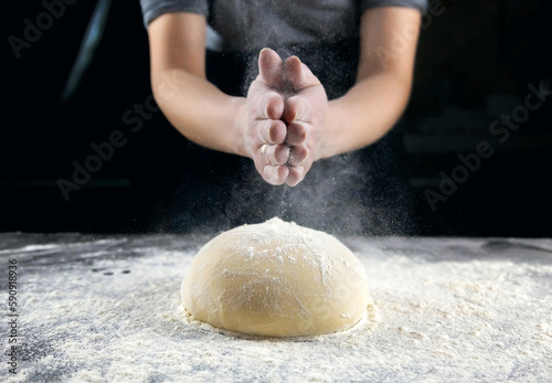 Making bread, kneading the dough. Hands on a dark background sprinkle flour on brightly lit dough.
