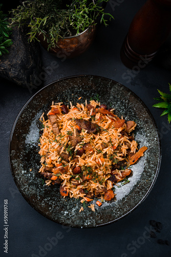 Pilaf with with lamb, raisins, almonds, carrots, tomatoes, onions and herbs on dark background.