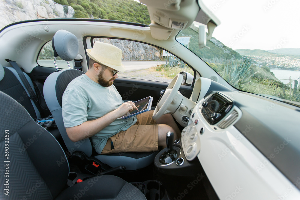 Hipster man looking on location navigation map in car, tourist traveler driving and hold in male hands europe cartography, view and plan tourist way road, trip in transportation cabriolet auto Hipster man looking on location navigation map in car, tourist traveler driving and hold in male hands europe cartography, view and plan tourist way road, trip in transportation cabriolet auto