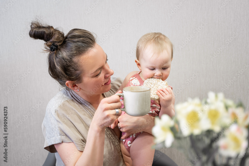 Family mother and cute baby eating breakfast at home child drinking from mother's cup. Infant tasting solid food, adult's meal. First steps Copy space Family mother and cute baby eating breakfast at home child drinking from mother's cup. Infant tasting solid food, adult's meal. First steps Copy space