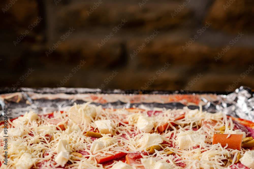 Cooking homemade pizza on baking sheet. Raw pizza on background of brick wall.