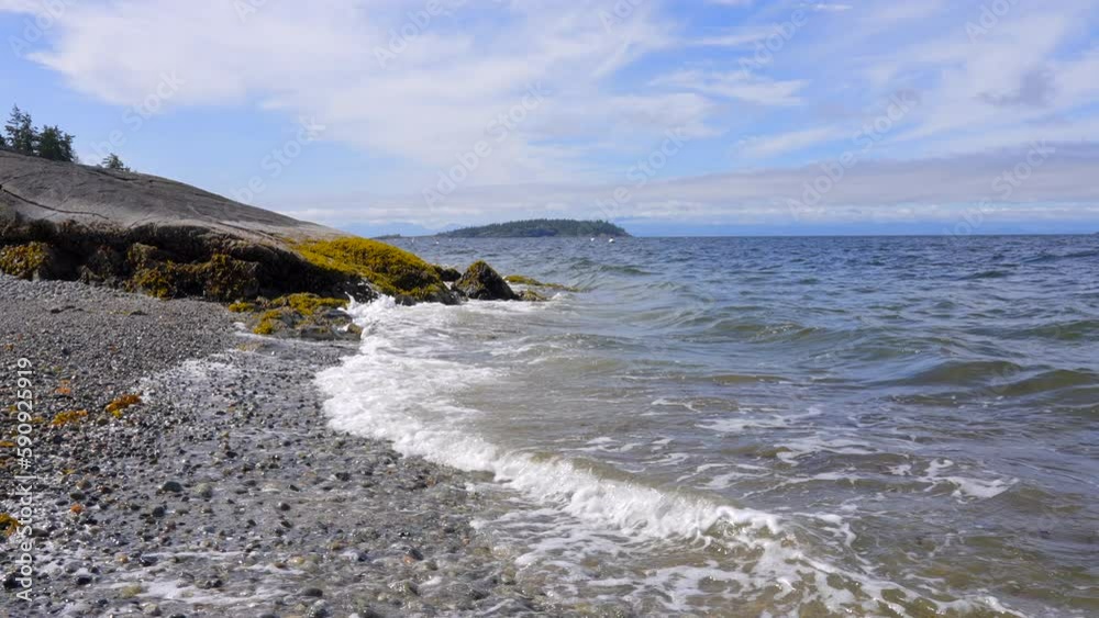 Establishing shot of ocean beach with rocks and pebbles in slow motion at summer day in Vancouver, Canada, North America. Day time on September 2022. Still camera. ProRes 422 HQ.