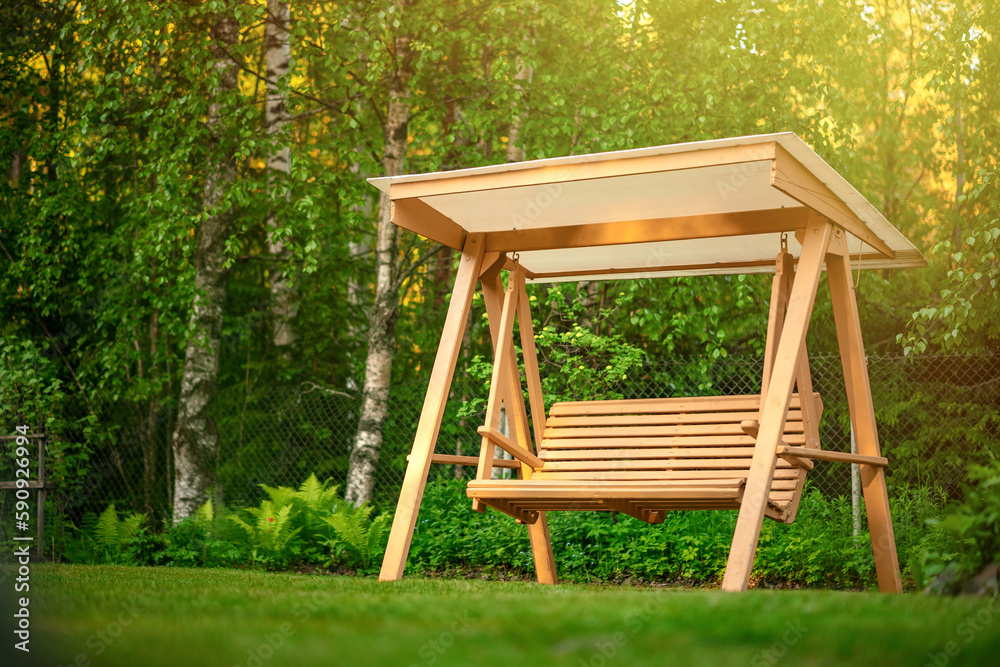 The garden swing stands in the green courtyard of a country house.Landscaping in the yard in summer. Furniture for home and garden. The garden swing stands in the green courtyard of a country house.Landscaping in the yard in summer. Furniture for home and garden.