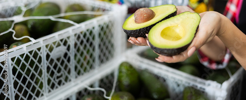 Hands of female worker in fruit sorting and packing warehouse holding two halves of cut ripe hass avocado photo