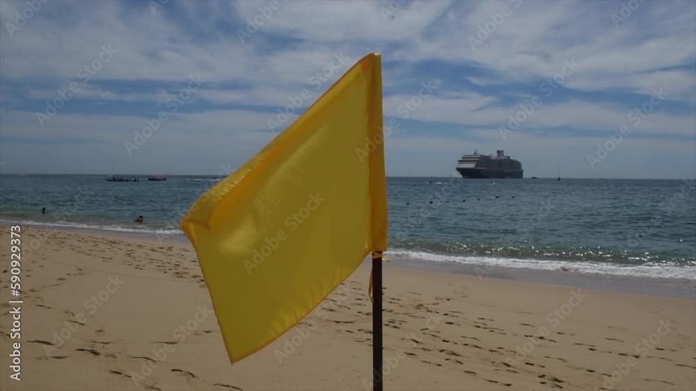 A slow motion of a yellow caution flag plowing in the breeze on quiet Cabo San Lucas Mexico beach. A slow motion of a yellow caution flag plowing in the breeze on quiet Cabo San Lucas Mexico beach.