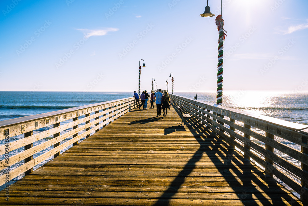 A long wooden pier, and walking people. Cayucos pier, California Central coast