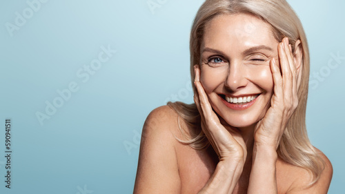 Beautiful gorgeous 50s mid aged mature woman looking at camera isolated on blue. Mature old lady close up portrait. Healthy face skin care beauty, middle age skincare cosmetics, cosmetology concept