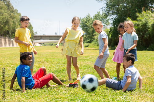 Group of happy schoolchildren playing football together in park