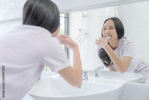 Happy Asian woman brushing her teeth with a toothbrush in the bathroom in bright morning.