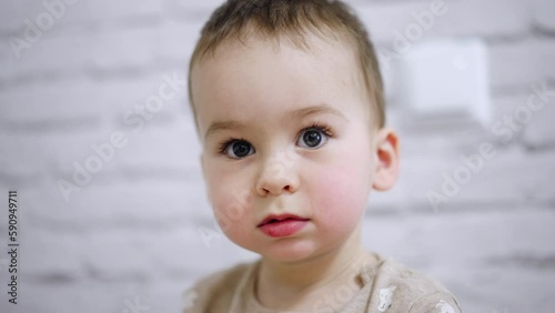 Adorable big-eyed baby boy with mousy hair. Portrait of a calm Caucasian kid focused on something. Close up. Blurred white backdrop.