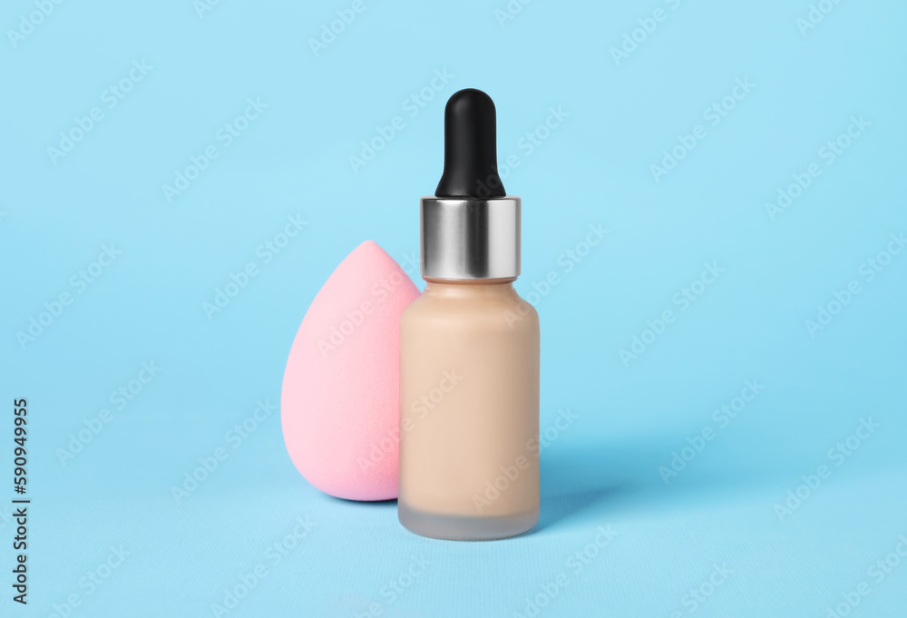 Bottle of skin foundation and sponge on light blue background. Makeup product Bottle of skin foundation and sponge on light blue background. Makeup product