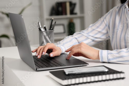 Woman working with laptop at white desk indoors, closeup