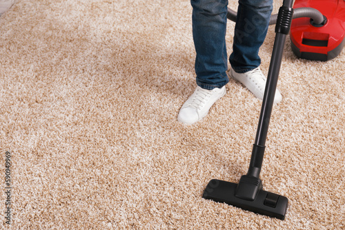 Man cleaning carpet with vacuum cleaner at home, closeup. Space for text