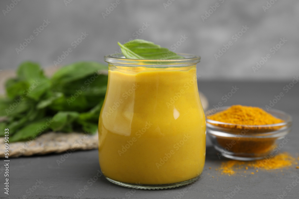 Tasty curry sauce, powder and basil leaves on grey table Tasty curry sauce, powder and basil leaves on grey table