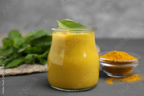 Tasty curry sauce, powder and basil leaves on grey table
