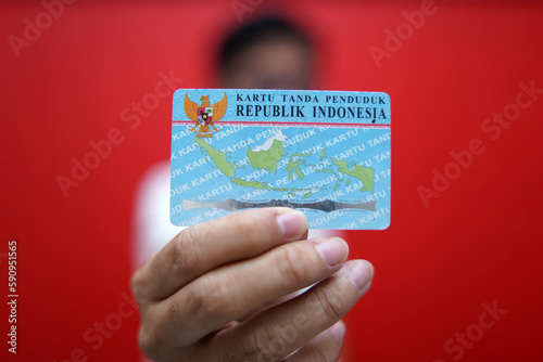 Fotografie A person showing and holding an Indonesian identity card (KTP) using a red t-shirt and a red background