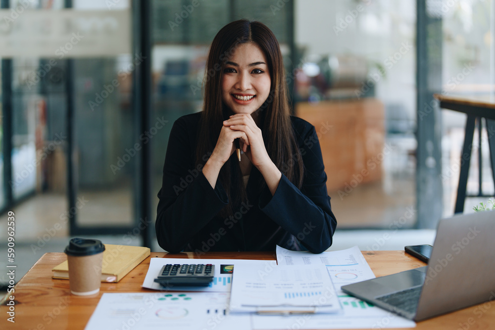Portrait of a woman business owner showing a happy smiling face as he has successfully invested her business using computers and financial budget documents at work Portrait of a woman business owner showing a happy smiling face as he has successfully invested her business using computers and financial budget documents at work