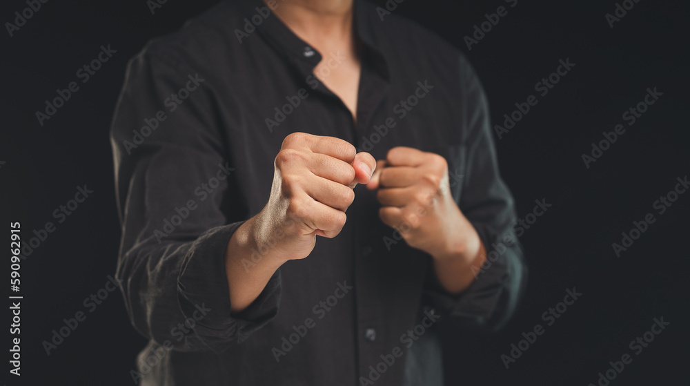 Fototapeta premium A man in a black shirt raised his fists while standing against a black background