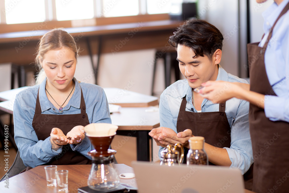 Young man and woman learning making coffee and sniff bean with barista while laptop on desk at cafe, group people training drip coffee with entrepreneur, small business or SME.