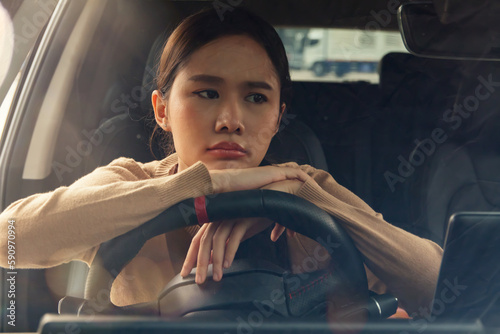 Asian woman with her hands on the steering wheel feeling exhausted, stressed with work, thinking about something and absentmindedly in the car while driving, looking outside with an indifferent face.