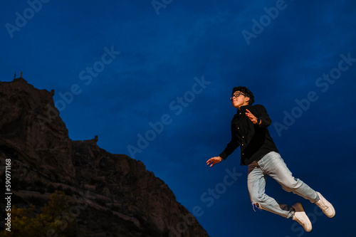 Young transgender man jumping outdoors at night. © Viviland