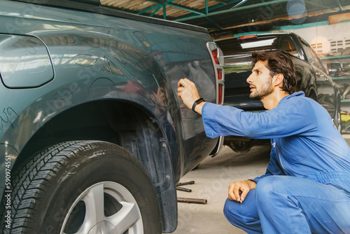 Male worker inspecting pickup truck, paint mechanic examining scratched car surface body damage near wheel arches using white chalk to paint circles to repair in auto workshop factory with insurance. photo