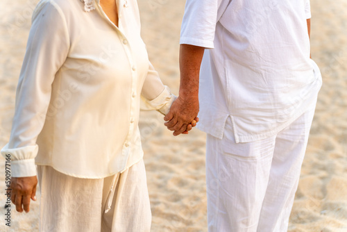 Happy Asian family senior couple with gray hair walking together at tropical beach at summer sunset. Retired elderly people enjoy romantic outdoor lifestyle travel nature ocean on holiday vacation.