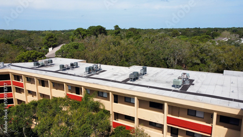 Aerial drone of apartment complex roof top with central air conditioning units with trees in Florida