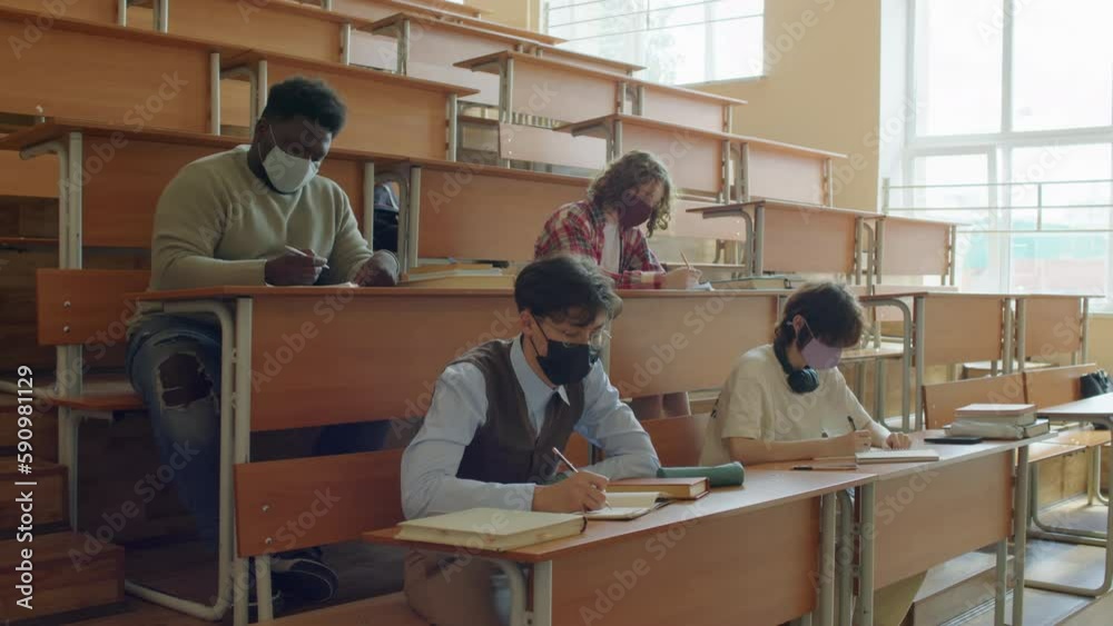 Group of ethnically diverse students wearing protective masks attending classes in college during quarantine Group of ethnically diverse students wearing protective masks attending classes in college during quarantine
