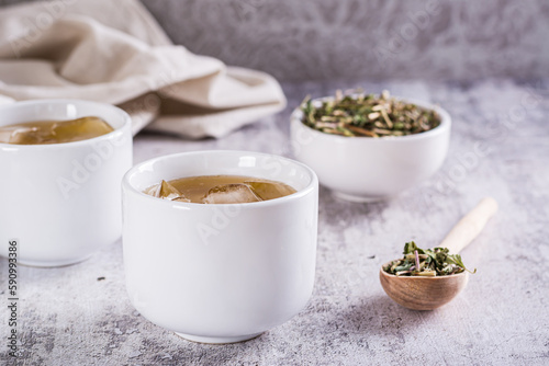 Cold green Japanese hojicha tea with ice in cups and dry tea in a bowl on the table