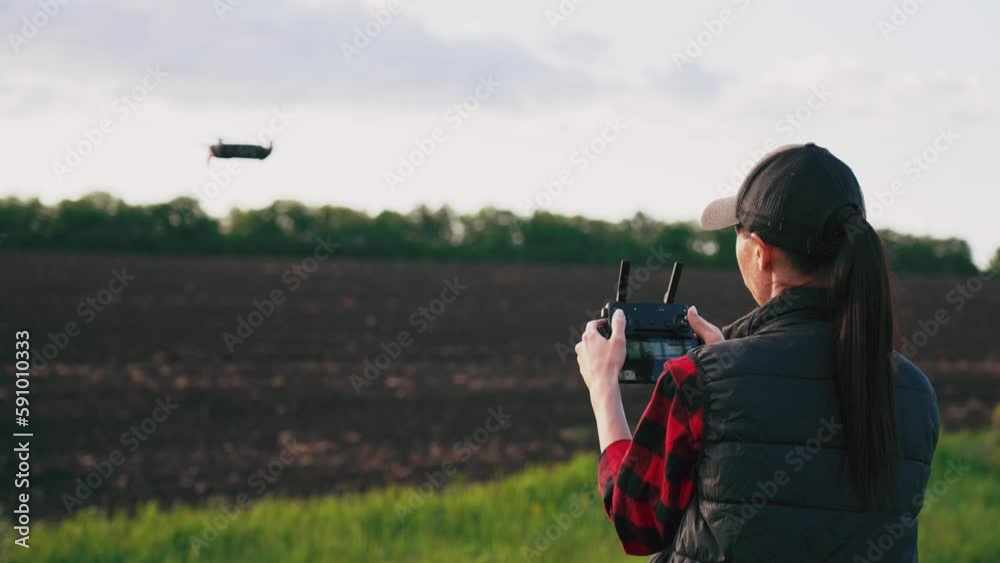 Woman farmer in hat standing in green wheat field and controlling of drone which flying above margin. Technologies in farming. Innovations for increasing productivity in agriculture. Woman farmer in hat standing in green wheat field and controlling of drone which flying above margin. Technologies in farming. Innovations for increasing productivity in agriculture.