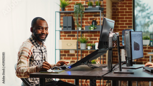 Happy content creator developing software interface on touchscreen display  using tablet and stylus at desk. African american man working on infographics production in agency studio.