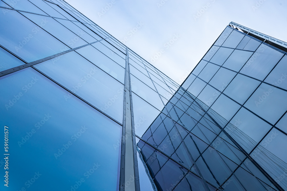 The blue sky is reflected in the windows of a modern office building. Architecture and exterior of contemporary houses