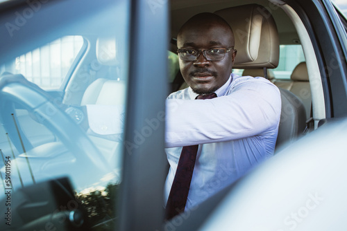 Portrait of a handsome African American businessman in a suit and glasses driving his new personal car