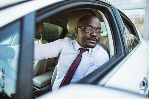 Portrait of a handsome African American businessman in a suit and glasses driving his new personal car © xartproduction