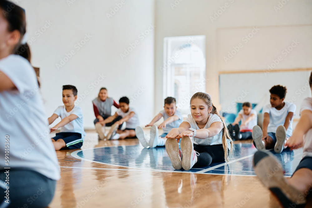 Schoolgirl and her classmates warming up during physical education class at school gymnasium. Schoolgirl and her classmates warming up during physical education class at school gymnasium.