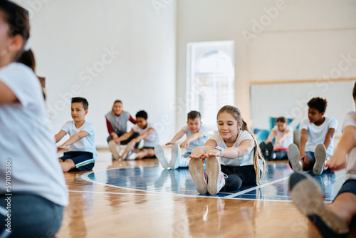Fototapeta Naklejka Na Ścianę i Meble -  Schoolgirl and her classmates warming up during physical education class at school gymnasium.