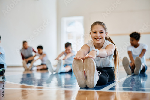 Stampa su tela Happy schoolgirl stretching during PE class and looking ta camera