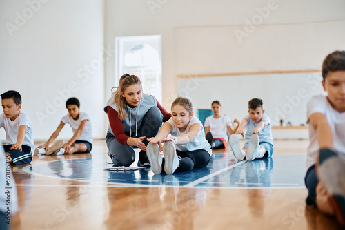 Little girl stretching with help of female coach during PE class at school.