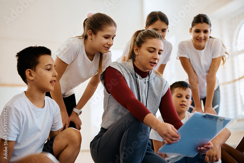 Fototapeta Naklejka Na Ścianę i Meble -  Female coach and group of kids analyzing game plan during PE class at school.
