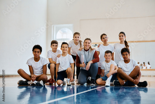 Portrait of happy sports teacher with group of kids at school gym looking at camera.