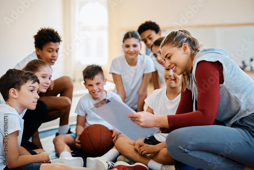 Happy PE teacher and her students planning basketball game strategy at school gym.