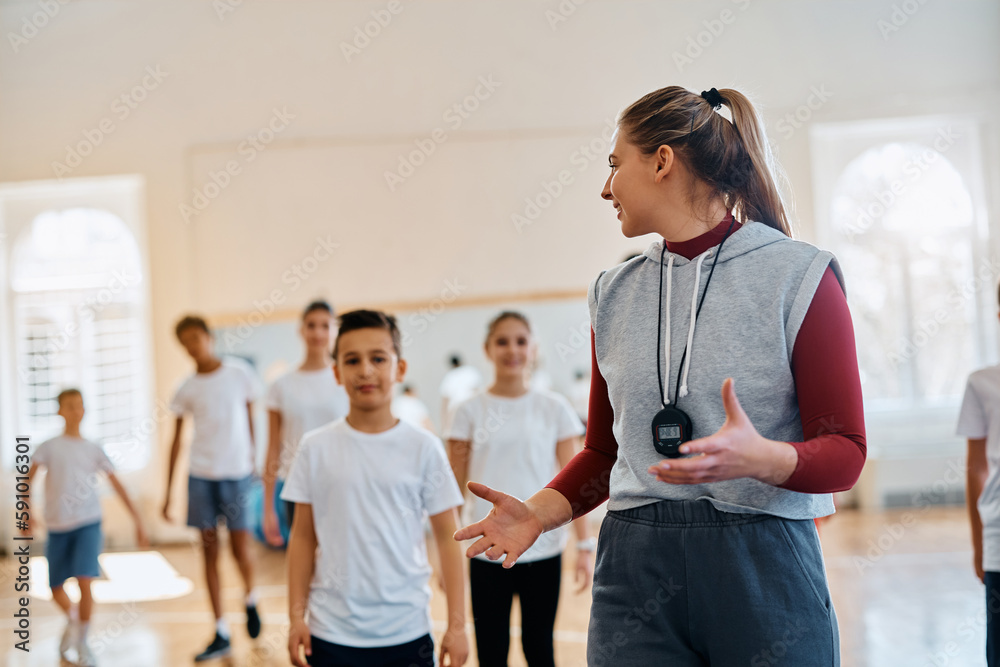 Happy physical education teacher talks to her students during exerise class at elementary school gym. Happy physical education teacher talks to her students during exerise class at elementary school gym.