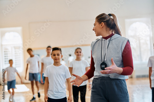 Happy physical education teacher talks to her students during exerise class at elementary school gym.