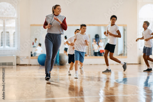 Happy PE teacher and group of kids running during exercise class at school gym.