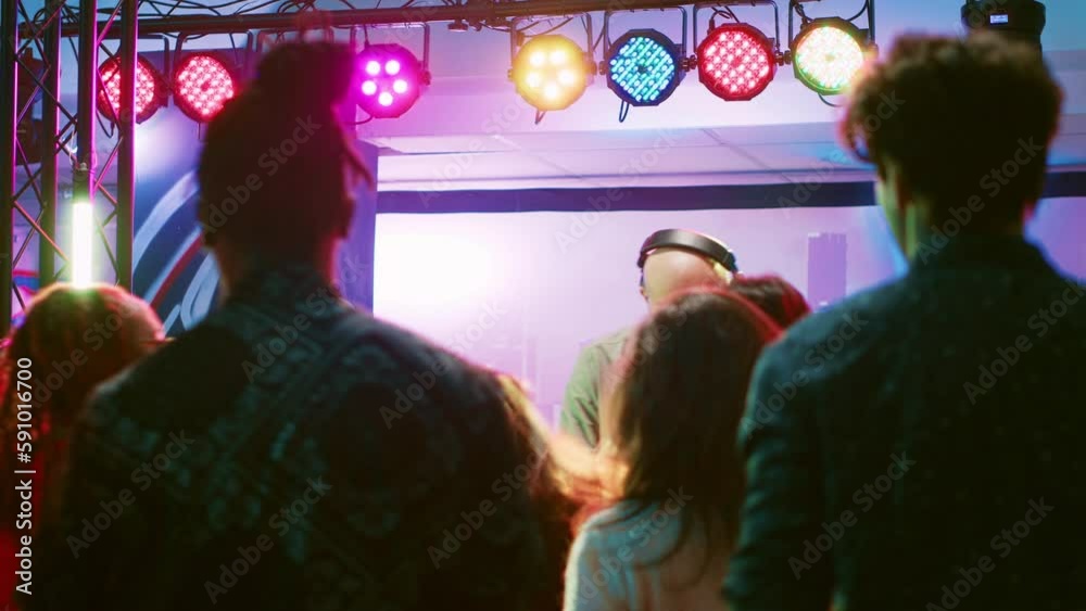 Male DJ putting music at club party, mixing electronic sounds at audio equipment station. Diverse group of friends jumping around and dancing on dance floor, clubbing entertainment. Male DJ putting music at club party, mixing electronic sounds at audio equipment station. Diverse group of friends jumping around and dancing on dance floor, clubbing entertainment.