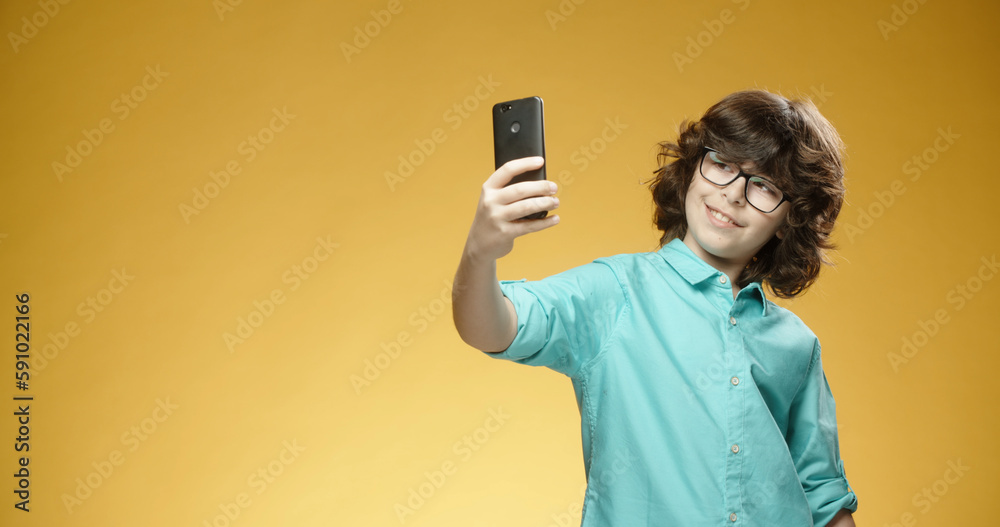 Cute little boy using his mobile phone to take pictures or selfies and positively smiling, isolated on yellow background - always online, emotions concept close up Cute little boy using his mobile phone to take pictures or selfies and positively smiling, isolated on yellow background - always online, emotions concept close up
