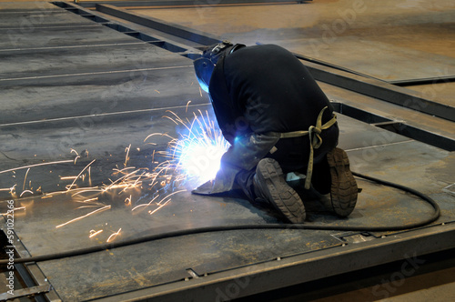 Welding process. A welder on his knees welds metal structures in a factory.