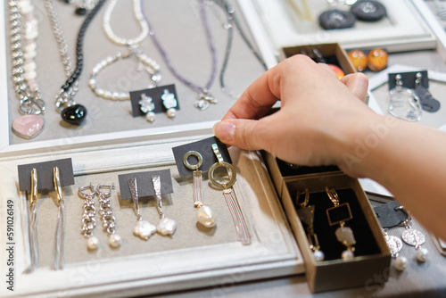 woman's hand delicately selects a handmade earring from a display, showcasing an array of artisanal jewelry in the background. supporting local artisans, and unique fashion accessories photo